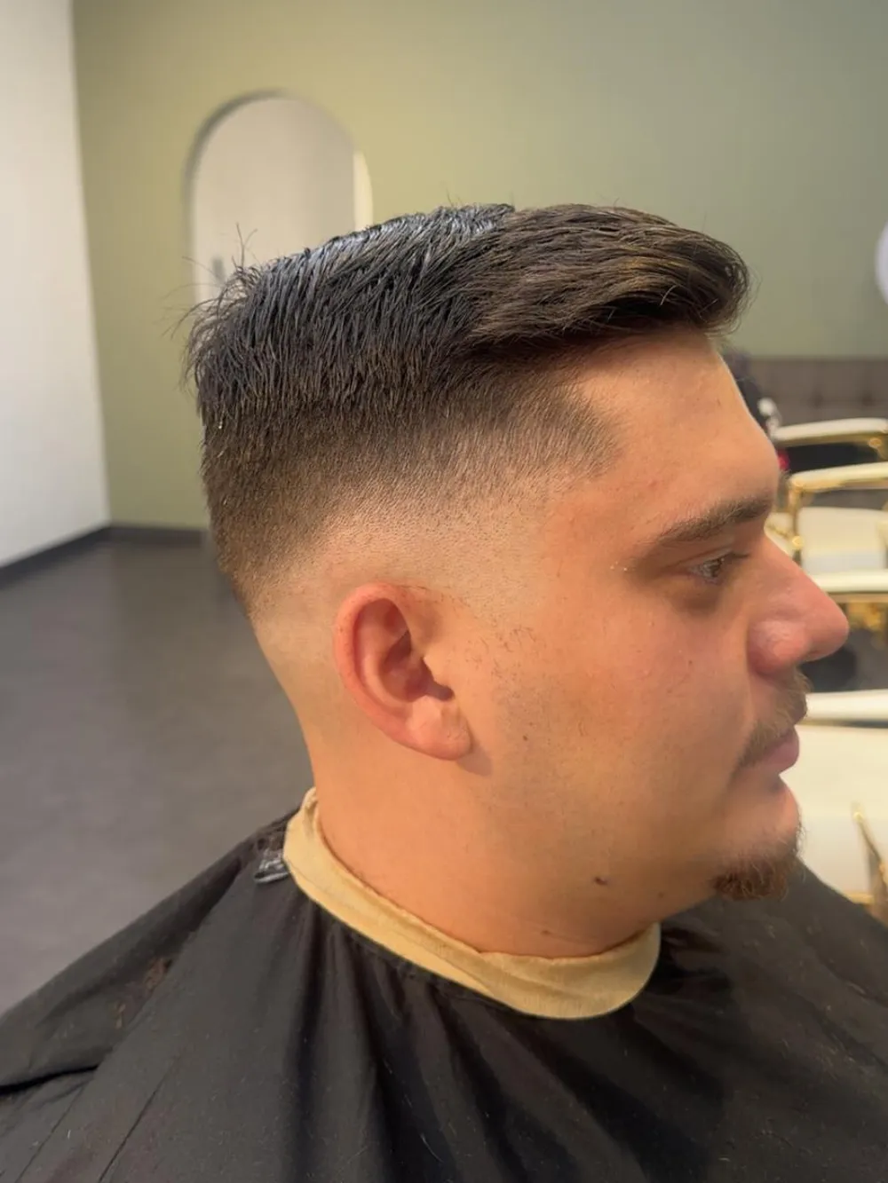 Herrenschnitt, hoher Fade an der Seite, längeres Deckhaar nach hinten frisiert.
